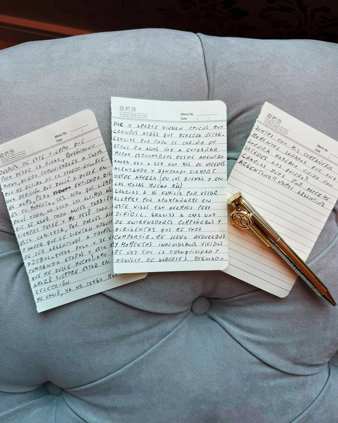 Three handwritten notebook pages and a pen on a grey tufted cushion, the pages carrying Lionel Messi's Spanish-language retirement letter.
